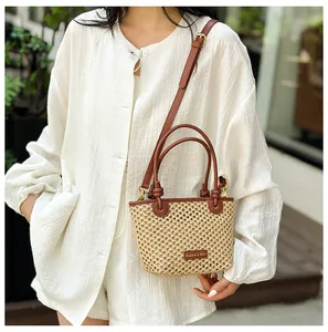 Detail of woven straw bucket bag with brown leather handles and adjustable shoulder strap