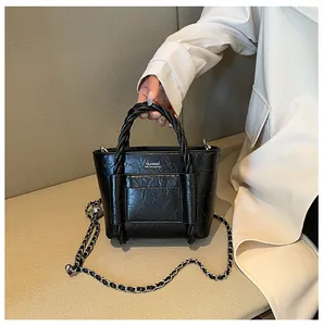 Detail of black textured bucket bag with woven handle and silver chain strap