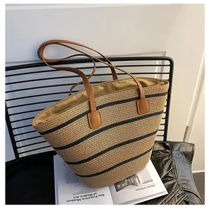 Detail of a woven straw tote bag with black stripes and brown leather shoulder straps
