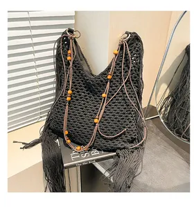 Detail van zwarte gehaakte hobo-tas met lange franjes en bruine houten kralen op de riem
