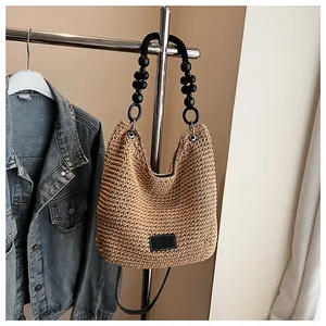 Light brown woven straw hobo bag with unique black wooden bead handle and leather patch