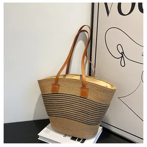 Detail of khaki straw tote bag featuring black stripes and brown leather handles on books