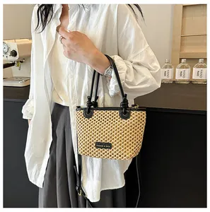 Detail of hand-woven beige bucket bag with black leather handles and logo plaque