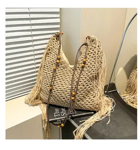 Detail van gehaakte beige strandtas met franjes en decoratieve houten kralen afwerking
