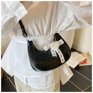 Detail of black faux leather crescent bag with white lace ribbon and pearl heart charm