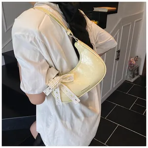 Detail of pale yellow crescent bag with lace bow and pearl charm on a model