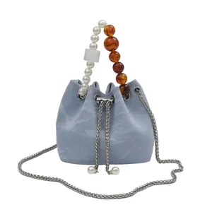 Bolso saco azul claro con textura plisada, asa de perlas y correa de cadena plateada