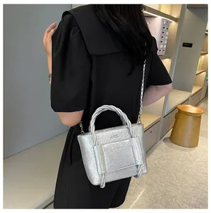 Detail of silver metallic mini bag with pleated texture and woven knot handle on model