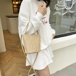 Beige geweven stro emmer tas met lederen riem getoond in een chique outdoor cafe setting