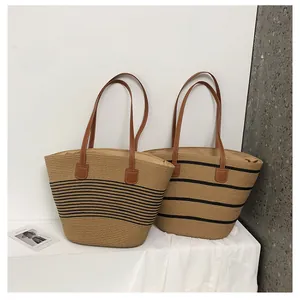 Detail view of woven straw tote bags with brown leather handles and black stripe patterns