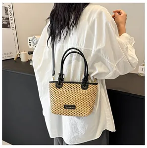 Detail of straw bucket bag featuring black leather handles and long crossbody strap