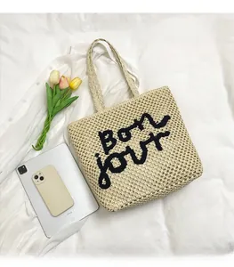 Detailed view of beige straw tote bag with black Bonjour embroidery and hollow mesh weave