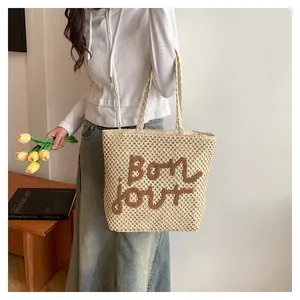 Detail of off-white woven tote with brown plush Bonjour lettering and double handles