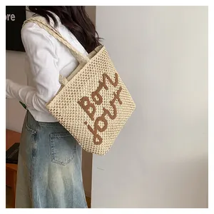 Close-up detail of cream woven straw tote bag with brown embroidered bon jour lettering
