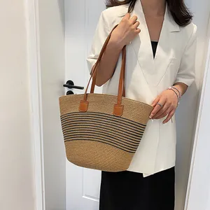 Straw tote bag with black stripes and brown leather straps worn by model against a white wall