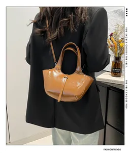 Schicke karamellfarbene Eimertasche aus Lackleder, von Model in modernem Büro gehalten