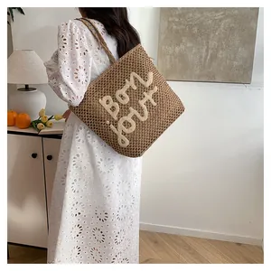 Detail view of woven straw tote bag with Bonjour embroidery and braided rope handle