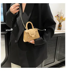 Detail einer hellbraunen Mini-Handtasche mit Goldnieten und Perlenkette am Model