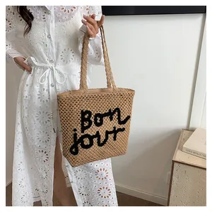 Detail of hollow woven straw tote bag featuring black Bon jour embroidery and large cutout mesh