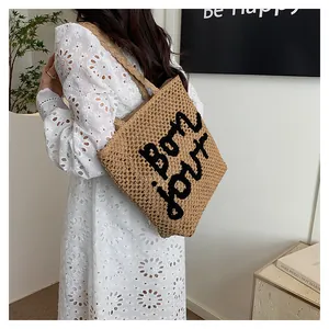 Detail of hollow woven straw tote bag with black bon jour lettering on model