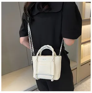Detail of off-white textured bucket bag with woven handles and silver chain strap