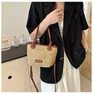 Detailed view of beige straw bucket bag with brown leather straps worn by a model