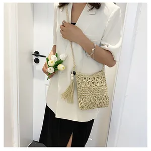 Detailed shot of beige hollow-out straw crossbody bag with elegant tassels on a model