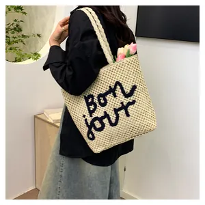 Detail of hand-woven beige straw tote bag featuring black Bonjour lettering and texture