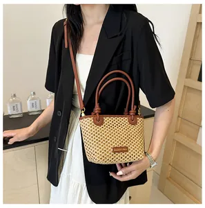 Straw bucket bag with brown leather handles worn by model in minimalist indoor setting
