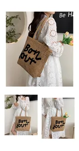 Detail showing the black embroidered Bon jour text on the beige handwoven straw tote bag