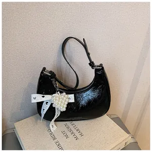 Detail of black glossy crescent bag with lace bow and pearl heart charm accessory
