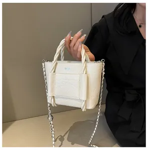 Detail of cream-colored pleated handbag with thick twisted handles and chain strap