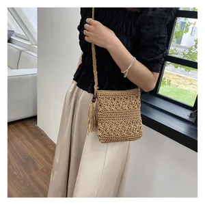 Detail of straw woven crossbody bag with hollow patterns and wooden bead tassel