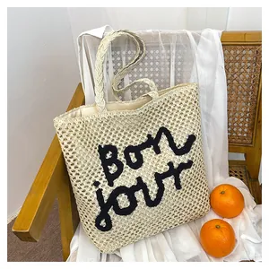 Detail of hand-woven straw tote bag with black embroidered Bonjour text on front