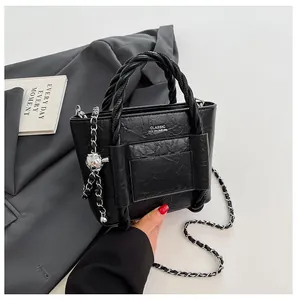 Detail of black textured bucket bag with woven handle and chain strap on grey blazer