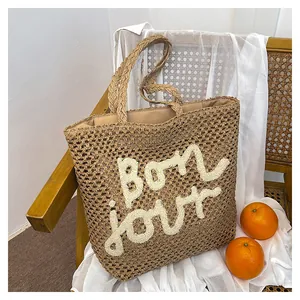 Close-up of woven straw tote bag with plush 'bon jour' lettering on a wooden chair