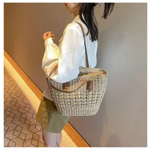 Detail of hand-woven straw tote bag with brown leather straps shown on a shoulder