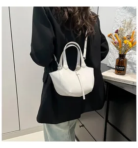 Detailansicht einer weißen Eimer-Tasche mit silbernen Details auf schwarzem Blazer