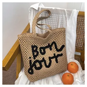 Detailed close-up of woven straw tote bag with black Bonjour embroidery on a wooden chair