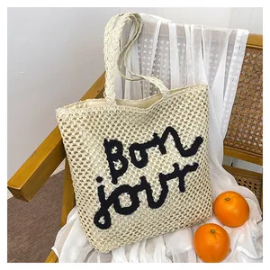 Detailed view of straw tote bag with Bonjour embroidery and hollow-out weave texture