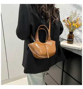 Detailaufnahme der glänzenden Leder-Eimertasche mit geometrischem Schnitt in Karamell
