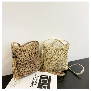 Detail of straw woven crossbody bag featuring floral hollow pattern and boho tassels