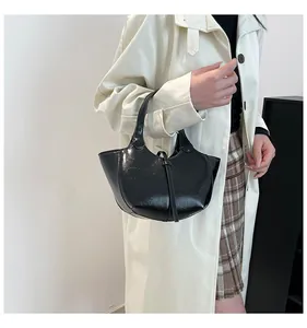Detail einer glänzend schwarzen Handtasche kombiniert mit einem beigen Trenchcoat