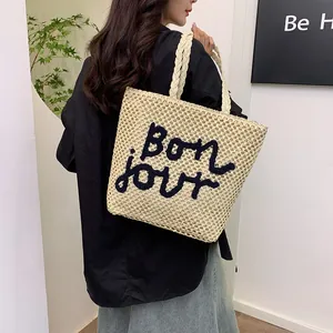 Straw tote bag with Bonjour embroidery shown on a model with denim skirt for beach vacation