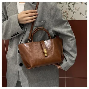 Detail of vintage brown oil wax leather bag with elegant gold metal lock on grey suit