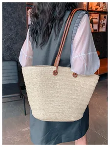 Détail du sac cabas en paille tissée avec des bandoulières en cuir marron sur un mannequin