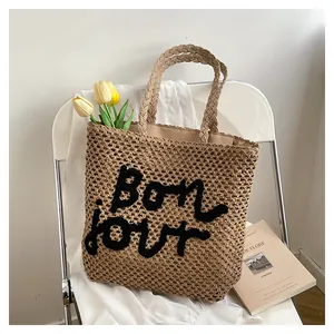 Chic beige hollow straw tote bag with black Bonjour embroidery on a white chair