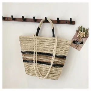 Détail du sac cabas en paille tissée avec doubles anses et rayures sur un mur blanc