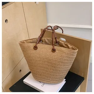 Détail d'un sac cabas en paille tissée avec anses en cuir marron et anneaux en métal