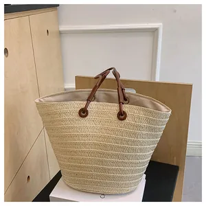 Gros plan sur la texture en paille tressée et l'anse en cuir marron d'un sac cabas d'été